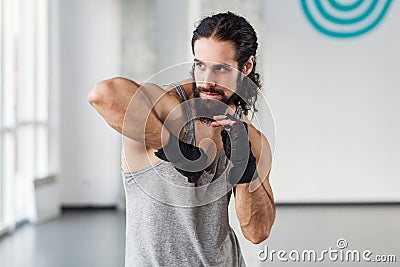 Portrait of angry muscular young adult man with curly hair standing and preparing to fight with elbow in black gloves, showing Stock Photo