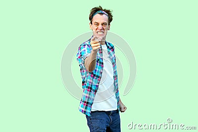 Portrait of angry nervous young man in casual blue checkered shirt and headband standing, clenching teeth, blaming and looking at Stock Photo