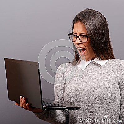 Portrait of angry woman screaming at her laptop against gray background Stock Photo