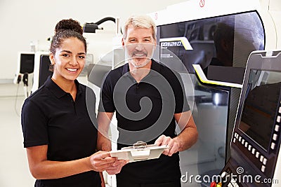 Portrait Of Apprentice Working With Engineer On CNC Machine Stock Photo