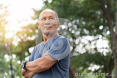 Portrait of Asian Elderly man with arms crossed relaxing over nature background. Happy confident Senior person in blue shirt Stock Photo