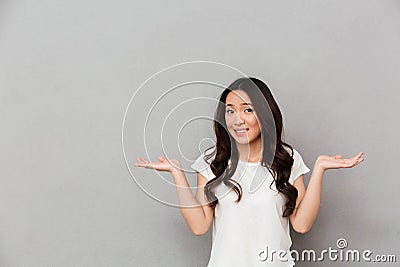 Portrait of asian indecisive woman with dark curly hair shrugging and throwing hands aside with clueless, isolated over gray back Stock Photo