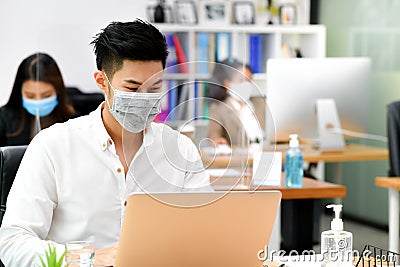 Portrait of Asian man office worker wearing face mask working in new normal office and doing social distancing during corona virus Stock Photo