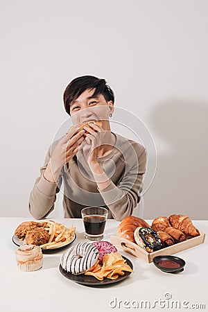 Portrait of asian man sitting and snacking donuts isolated over white background. Fat man diet concept Stock Photo