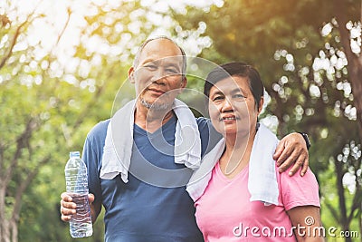 Portrait of Asian Senior couple in blue and pink shirt smiling and standing at park outdoor Stock Photo