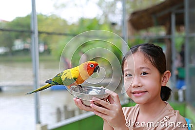 Portrait of Asian young girl child holding Aluminium bowl feeding macaw bird animal in the zoo Stock Photo