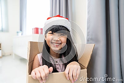 Portrait of Asian young girl kid wear Santa hat and sit in gift box. Little adorable child feel excited and happy to celebrate Stock Photo