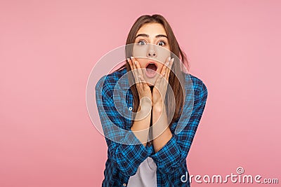 Portrait of astonished emotional funny girl in checkered shirt looking with big eyes, holding hands on face Stock Photo