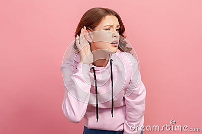 Portrait of attentive brunette teen girl in hoodie holding hand near ear trying to listen quiet conversation, overhearing gossip Stock Photo