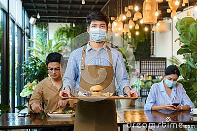 Portrait attractive asian waitress wear face mask and face shield holding food tray to serving meal to customer with custome in Stock Photo
