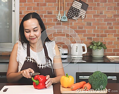 Attractive Asian woman cooking in the kitchen with vegetable, capsicum, carrot and Broccoli. cutting capsicum, smiling happily. Stock Photo