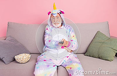 Portrait of attractive bored grey-haired man sitting on divan watching video series isolated over pink color background Stock Photo