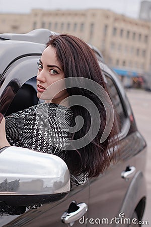 portrait of attractive brunette in grey checkered dress in a black car. girl in automobile. business woman Stock Photo