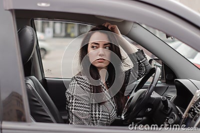 portrait of attractive brunette in grey checkered dress in a black car. girl in automobile. business woman Stock Photo