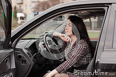 portrait of attractive brunette in grey checkered dress in a black car. girl in automobile. business woman Stock Photo