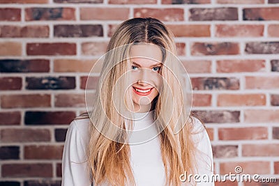 Portrait of attractive charming young blonde woman with long hair on red brick background. Cute coed girl smiles and looks at the Stock Photo