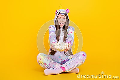 Portrait of attractive cheerful amazed girl sitting lotus pose eating giving you corn isolated over bright yellow color Stock Photo