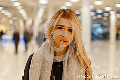 Portrait of an attractive cute young blonde woman with sexy lips with beautiful gray eyes in a coat in a vintage scarf indoors. Stock Photo