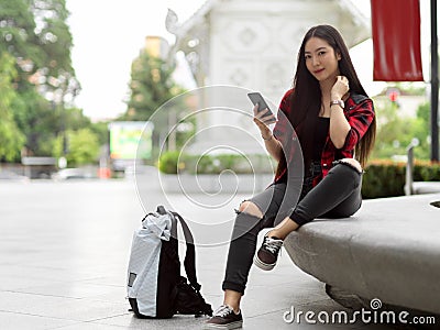 Portrait of attractive female backpacker posing with smartphone on city street Stock Photo