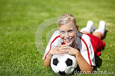 Shes the team captain. Portrait of an attractive female football player lying chest down on the grass and leaning on a Stock Photo