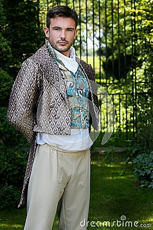 Portrait of handsome gentleman dressed in vintage costume standing in stately home courtyard with railings in background Stock Photo