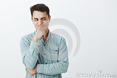 Portrait of attractive male villain in casual clothes, holding hand on chin and looking right with smirk and nasty Stock Photo