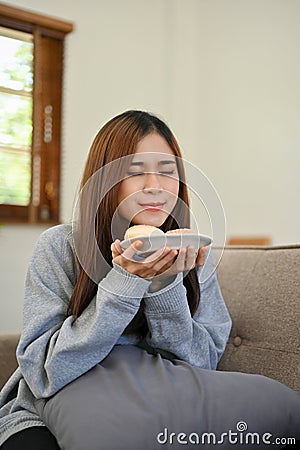 Portrait, Attractive Asian girl smelling doughnuts, tasting yummy doughnut Stock Photo