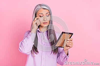 Portrait of attractive sad sullen gray-haired woman looking at photo crying isolated over pink pastel color background Stock Photo