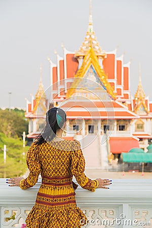 Portrait back side Asian woman in a yellow Thai patterned standing in front of a Buddhist Chruch while traveling in Asia Stock Photo