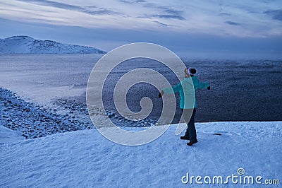 Portrait from back of warmly dressed woman in defocus standing in front of sea looking far away looking at winter rough Stock Photo