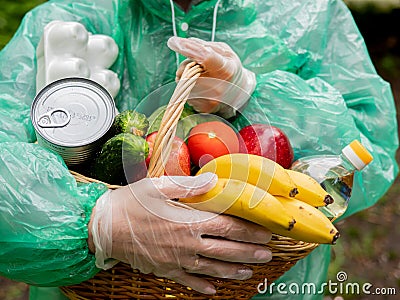 Portrait of a basket of food in the hands of a woman volunteer in protective gloves and rain coat, close-up. Stock Photo