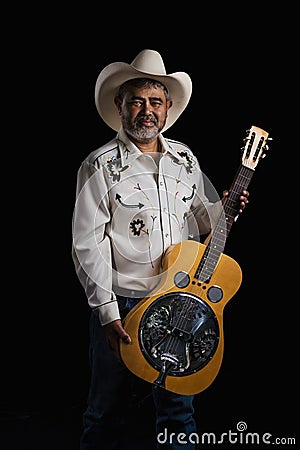 Portrait of bearded Asian musician dons cowboy attire, clutching a Dobro guitar on a black backdrop Stock Photo