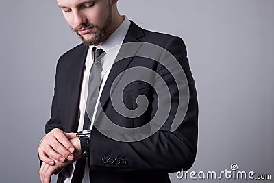 Portrait of a bearded guy, twenty-five years old, in a business suit, looks at his watch. Simple minimalistic business concept. On Stock Photo