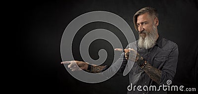 Portrait of a bearded hipster, who is pointing with his fingers to something, isolated on a black background Stock Photo