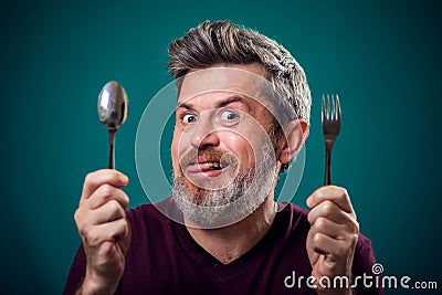 A portrait of bearded man holding spoon and fork in hands. People and food concept Stock Photo