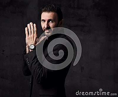 Portrait of bearded mature businessman in jacket with mandarin collar stands sideways with hands put together Stock Photo