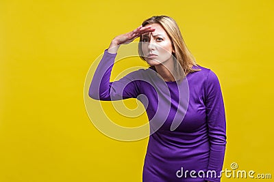 Portrait of beautiful ambitious woman watching far away with hand above eyes. indoor studio shot isolated on yellow background Stock Photo