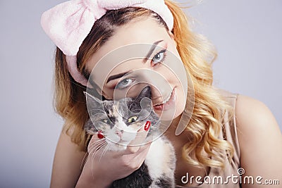 Portrait of a beautiful cute girl with a cat in hands,young woman in a headband for make up on a gray studio background with a Stock Photo