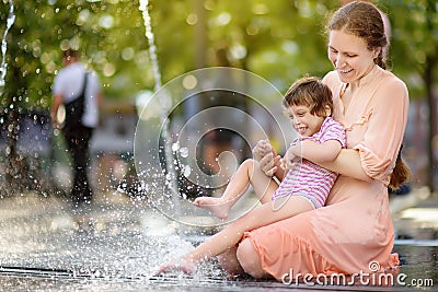 Portrait of beautiful disabled girl in the arms of his mother having fun in fountain of public park at sunny summer day. Child Stock Photo