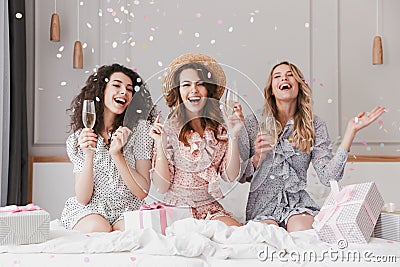 Portrait of beautiful excited women 20s wearing dresses celebrating bridal shower in posh apartment, with champagne and falling c Stock Photo