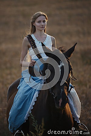 Portrait of a beautiful female cowgirl with shotgun from wild west riding a horse in the outback. Stock Photo