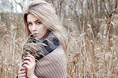 Portrait of a beautiful girl with blue eyes in a grey jacket in the field among trees and tall dry grass, tinted in shades of gray Stock Photo