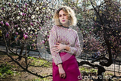 Portrait of beautiful girl with curly long hair in pink blouse walks in garden of magnolias Stock Photo