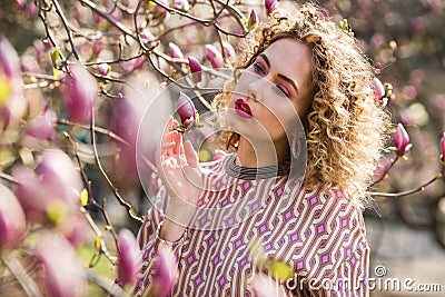 Portrait of beautiful girl with curly long hair in pink blouse walks in garden of magnolias Stock Photo
