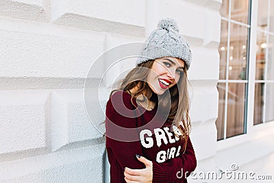 Portrait beautiful girl with long hair in marsala sweater on grey wall background outside. She wears knitted hat, red Stock Photo