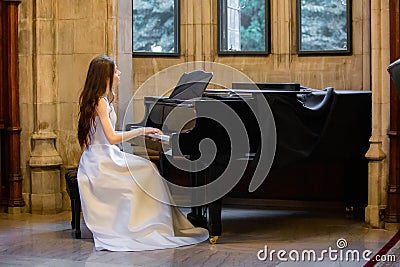 Portrait of a beautiful girl wearing white wedding dress at the piano playing Stock Photo