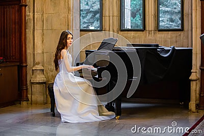 Portrait of a beautiful girl wearing white wedding dress at the piano playing Stock Photo