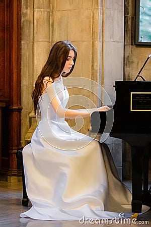 Portrait of a beautiful girl wearing white wedding dress at the piano playing Stock Photo