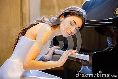 Portrait of a beautiful girl wearing white wedding dress at the piano playing Stock Photo