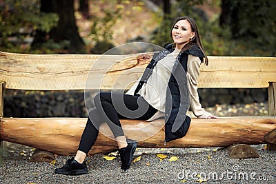Portrait of a beautiful happy young tatar woman in full growth sitting on a wooden bench in a park outdoors Stock Photo